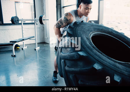 Junge Sportler spiegeln schwere Reifen im Fitnessstudio konzentriert Stockfoto