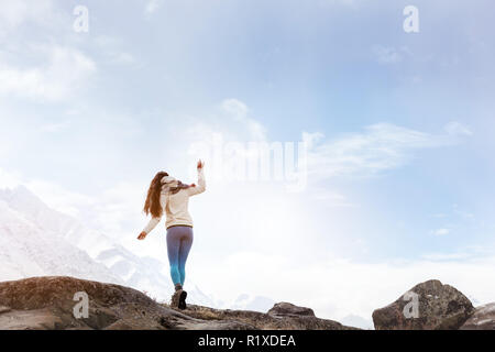 Dame ist zu Fuß durch große Felsen auf dem Hintergrund der schneebedeckten Berge Stockfoto