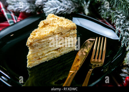 Köstliche puste Kuchen mit Krümel abgedeckt. Leckeren Nachtisch essen in Nahaufnahme. Dessert serviert auf schwarze Platte, dekoriert mit Tannenzweigen. Französische Küche. Christus Stockfoto