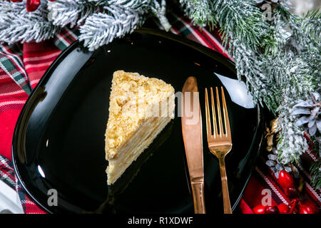 Köstliche puste Kuchen mit Krümel abgedeckt. Leckeren Nachtisch essen in Nahaufnahme. Dessert serviert auf schwarze Platte, dekoriert mit Tannenzweigen. Französische Küche. Christus Stockfoto