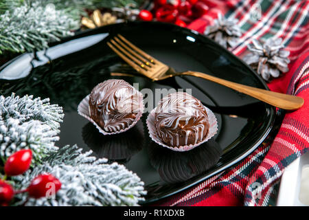 Leckere dunkle Schokolade Kuchen bedeckt mit verglast. Leckeren Nachtisch essen in Nahaufnahme. Chocolate desserts serviert auf schwarze Platte, dekoriert mit Tannenzweigen. Stockfoto