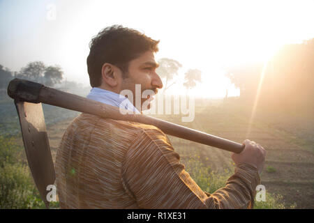 Seitenansicht eines Bauern in seiner Landwirtschaft Feld mit einem Spaten auf seiner Schulter mit Sonne in den Hintergrund. Stockfoto