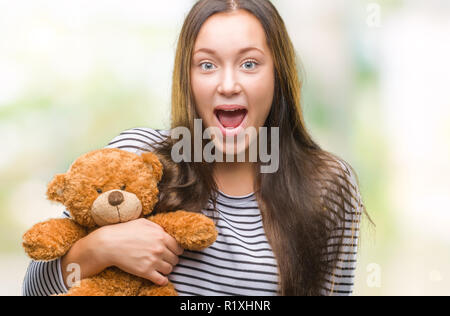 Junge kaukasier Frau mit Teddybär über isolierte Hintergrund im Schlag mit einer Überraschung konfrontiert, ängstlich und aufgeregt mit Angst Angst Ausdruck Stockfoto