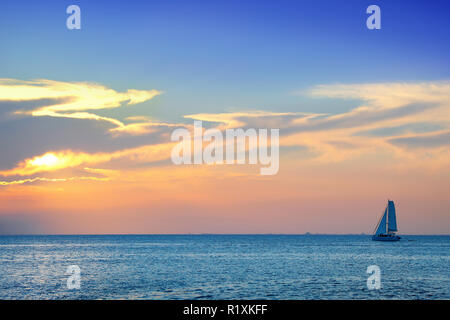 Bunte seascape Bild mit glänzenden Meer und Segelboot über bewölkten Himmel und Sonne bei Sonnenuntergang in Cozumel, Mexiko Stockfoto