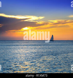 Bunte seascape Bild mit glänzenden Meer und Segelboot über bewölkten Himmel und Sonne bei Sonnenuntergang in Cozumel, Mexiko Stockfoto