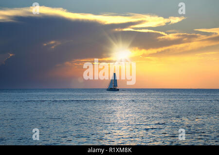 Bunte seascape Bild mit glänzenden Meer und Segelboot über bewölkten Himmel und Sonne bei Sonnenuntergang in Cozumel, Mexiko Stockfoto