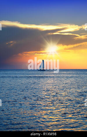 Bunte seascape Bild mit glänzenden Meer und Segelboot über bewölkten Himmel und Sonne bei Sonnenuntergang in Cozumel, Mexiko Stockfoto