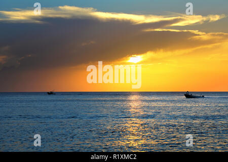 Bunte seascape Bild mit glänzenden Meer und Schnellboot über bewölkten Himmel und Sonne bei Sonnenuntergang in Cozumel, Mexiko Stockfoto