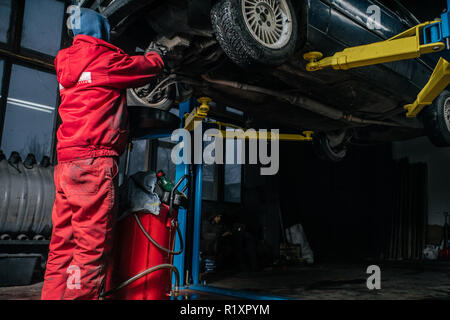 Jungen kaukasischen Mann in Rot Arbeitskleidung Reparatur Auto mit professionellen Werkzeugen Stockfoto