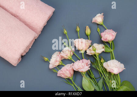 Weiche Frotteetücher mit Blumenstrauß aus roten Rose Blume auf grauem Hintergrund. Ansicht von oben. Stockfoto