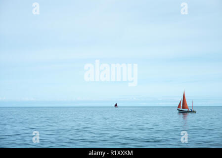 Yachten - Sportboote mit roten Segeln Segeln auf dem Wasser der Stille Ozean morgens um Aberaeron, Pembrokeshire, Wales, Großbritannien Stockfoto