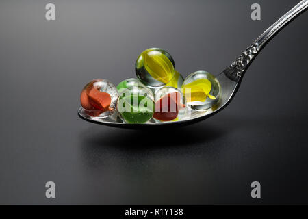 Farbige Kugeln aus Glas in einem metalllöffel Closeup auf einem dunkelgrauen Hintergrund Stockfoto