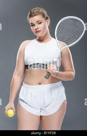 Attraktive übergewichtige Frau mit Tennis racquet Ball isoliert auf Grau Stockfoto