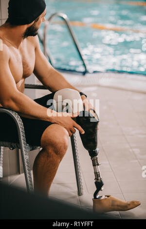 Happy Sportler mit künstlichen Bein sitzen auf Stuhl bei Hallenbad Stockfoto