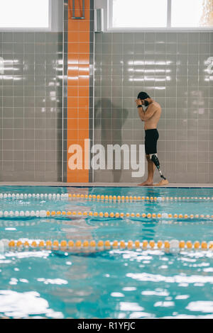 Hübscher junger Sportler mit künstlichen Bein zu Fuß durch am Pool im Hallenbad Stockfoto