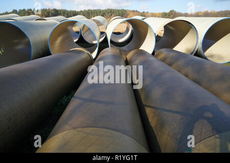 Große Kanalrohre liegen auf Sand und Schmutz in einem Herbst Wald Baustelle. Sonnige Oktober Tag outoor industrielle Schüsse Stockfoto