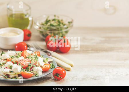 Gesund lecker lecker Salat mit Tomaten, Radieschen, Käse, Sprossen und Sesam in der Platte auf hellem Holztisch, flacher Tiefe des Feldes. Stockfoto