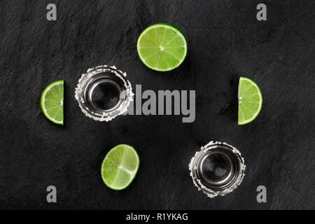 Ein Foto von Tequila shots mit Limetten, geschossen von oben auf einem schwarzen Hintergrund, bilden einen Rahmen mit einem Platz für Text