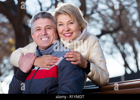 Positive Mann und Frau umarmen einander sitzen auf einer Parkbank Stockfoto