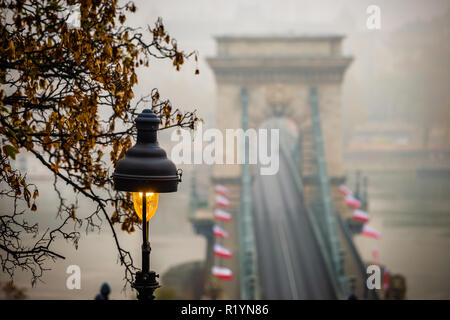 Budapest, Ungarn - Straße - Lampe mit Herbstlaub und berühmte Széchenyi Kettenbrücke im Hintergrund an einem nebligen Morgen im Herbst Stockfoto