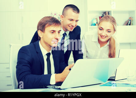 Drei freundlichen Business männlichen und weiblichen Kollegen in formale arbeiten mit Laptops und Sprechen in festen Büro Stockfoto