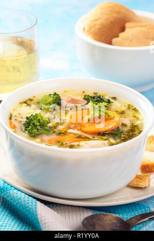 Italienische Gemüsesuppe mit Brokkoli Möhren Nudeln in Hühnerbrühe auf blauen Tisch mit Scheiben Brot und Glas Saft. Essen vegetarische organische noch Leben in hellem Stil close-up Stockfoto