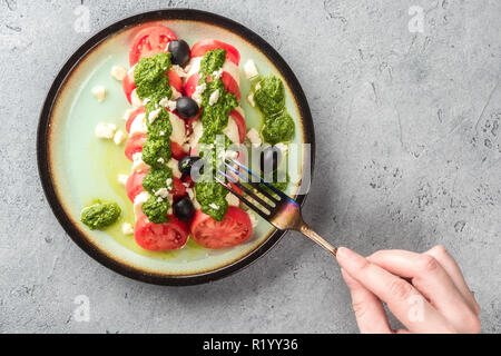 Tomaten und Mozzarella Caprese Salat und Pesto Sauce mit Oliven auf grau Tisch serviert mit Gabel. Essen italienische Vorspeise Stockfoto