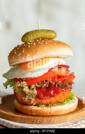 Burger mit gebratenen Eiern, Zwiebeln, Salat und Tomaten auf einer Holzplatte. Stockfoto