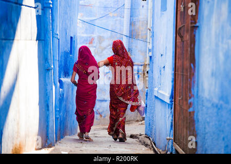 Zwei Frauen in der traditionellen indischen Sari gekleidet sind ein Spaziergang durch die engen Gassen von die blaue Stadt Jodhpur, Rajasthan, Indien.
