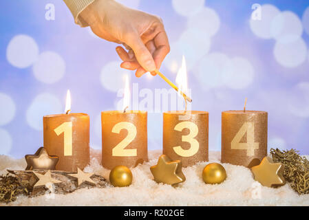 Vier nummerierten Gold advent Kerzen mit drei Kerzen von Hand mit Match- und Weihnachtsdekoration im Schnee liegend als Vorlage lit Stockfoto