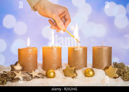 Vier gold advent Kerzen mit drei Kerzen von Hand mit Match- und Weihnachtsdekoration liegen im Schnee als Vorlage Stockfoto