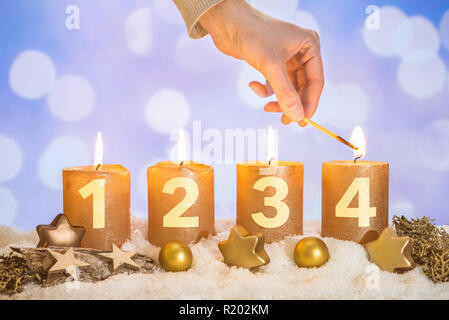 Vier nummerierten Gold advent Kerzen mit vier Kerzen von Hand mit Match- und Weihnachtsdekoration im Schnee liegend als Vorlage lit Stockfoto