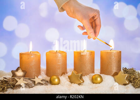 Vier gold advent Kerzen mit vier Kerzen von Hand mit Match- und Weihnachtsdekoration liegen im Schnee als Vorlage Stockfoto