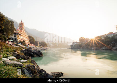 Spektakuläre Aussicht auf die Lakshman Jhula Brücke und dem schönen Tempel bei Sonnenuntergang in Rishikesh, Indien. Stockfoto