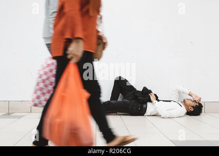 Junge asiatische Geschäftsmann liegend am Gehweg an sein Problem und suchen so depressiv, während Leute vorbei (Motion Blur) Stockfoto