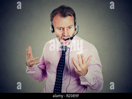 Erwachsenen Mann in das Arbeiten mit der Sprechgarnitur als Operator und brüllen sich Kunden auf grauem Hintergrund Stockfoto