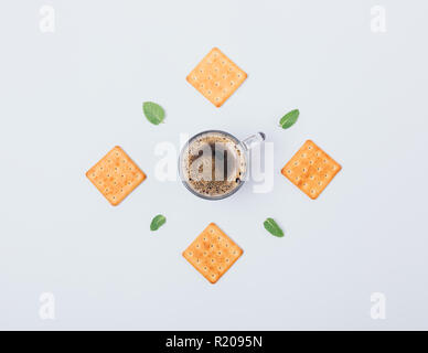 Flache Layout der Cracker, grüne Blätter und Tasse schwarzen Kaffee in der Mitte auf weißem Hintergrund. Ansicht von oben kreative Essen Zusammensetzung der Energie Frühstück. Stockfoto