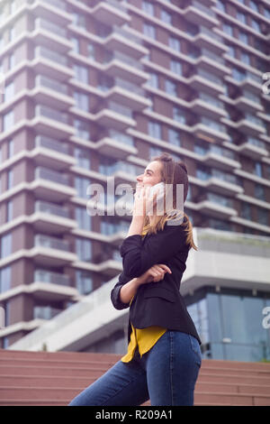 Junge Geschäftsfrau nutzt Handy auf der Straße gegen Bürogebäude Stockfoto