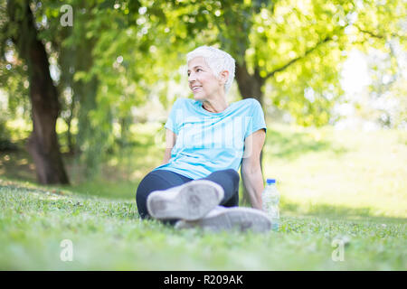 Ältere Frau Sitzen und Ausruhen nach Training im Park auf Gras Stockfoto