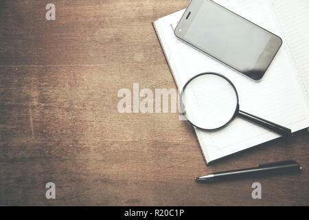 Notebook, Handy und Lupe auf hölzernen Tisch Stockfoto