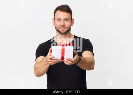Glückliche junge Mann mit einem Weihnachtsgeschenk auf weißem Hintergrund. Geschenk mit roter Schleife Stockfoto