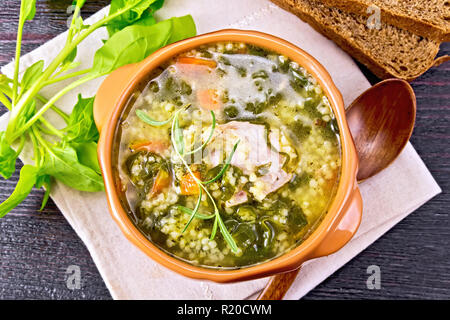 Schweinerippchen Suppe mit Couscous und Spinat in einer Schüssel auf Serviette, Brot auf Holzbrett Hintergrund von oben Stockfoto