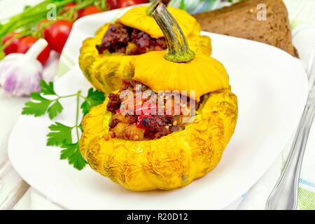 Zwei gelbe Zucchini gefüllt mit Fleisch, Tomaten und Paprika in die Schüssel, Brot, Knoblauch, Petersilie und eine Serviette auf einem hölzernen Brettern Hintergrund Stockfoto