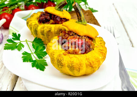 Zwei gelbe Zucchini gefüllt mit Fleisch, Tomaten und Paprika in die Schüssel, Brot, Knoblauch, Petersilie und Gabel auf dem Hintergrund Licht Holzbretter Stockfoto