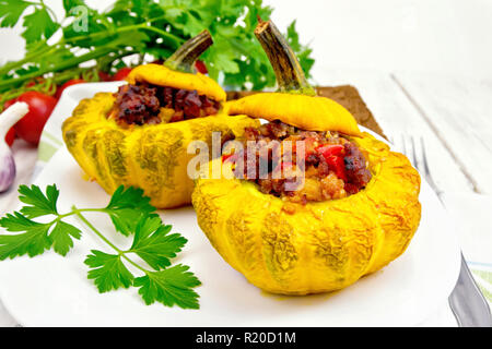 Zwei gelbe Zucchini gefüllt mit Fleisch, Tomaten und Paprika in die Schüssel, Brot, Knoblauch, Petersilie und Gabel auf dem Hintergrund der Holzbretter Stockfoto