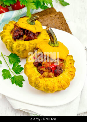 Zwei gelbe Zucchini gefüllt mit Fleisch, Tomaten und Paprika in die Schüssel, Brot, Petersilie und eine Serviette auf dem Hintergrund Licht Holzbretter Stockfoto