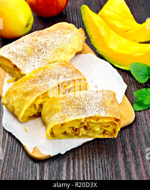 Strudel Kürbis und Apfel mit Rosinen auf Pergament, Früchte und Gemüse auf einem dunklen Holz- Board Stockfoto