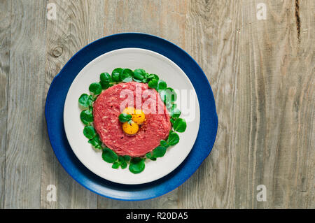 Blick von oben auf die Doppelte vergoldete Beef Steak Tartar mit drei rohe Wachtel Eigelb serviert und von Brunnenkresse Blätter auf einem Verwitterten grauen Holz- Eber umgeben Stockfoto