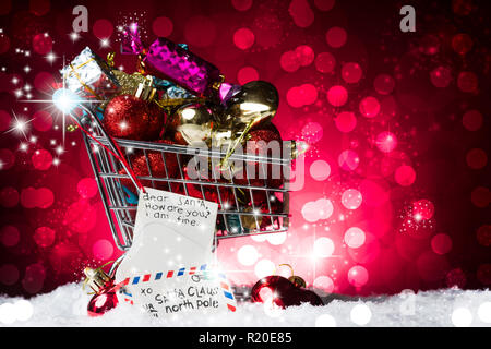 Christmas Shopping Konzept, eine Karre voller Geschenk und einen Brief an Santa Claus Dekoration, auf Schnee, gegen eine wunderschöne rote bokelicious Hintergrund Stockfoto