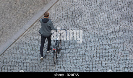 Luftaufnahme von einer Fußgängerzone tausendjährigen mit einem Fahrrad zu Fuß auf einer Straße mit Kopfsteinpflaster, im Gespräch auf mobilen, kopieren Raum Stockfoto